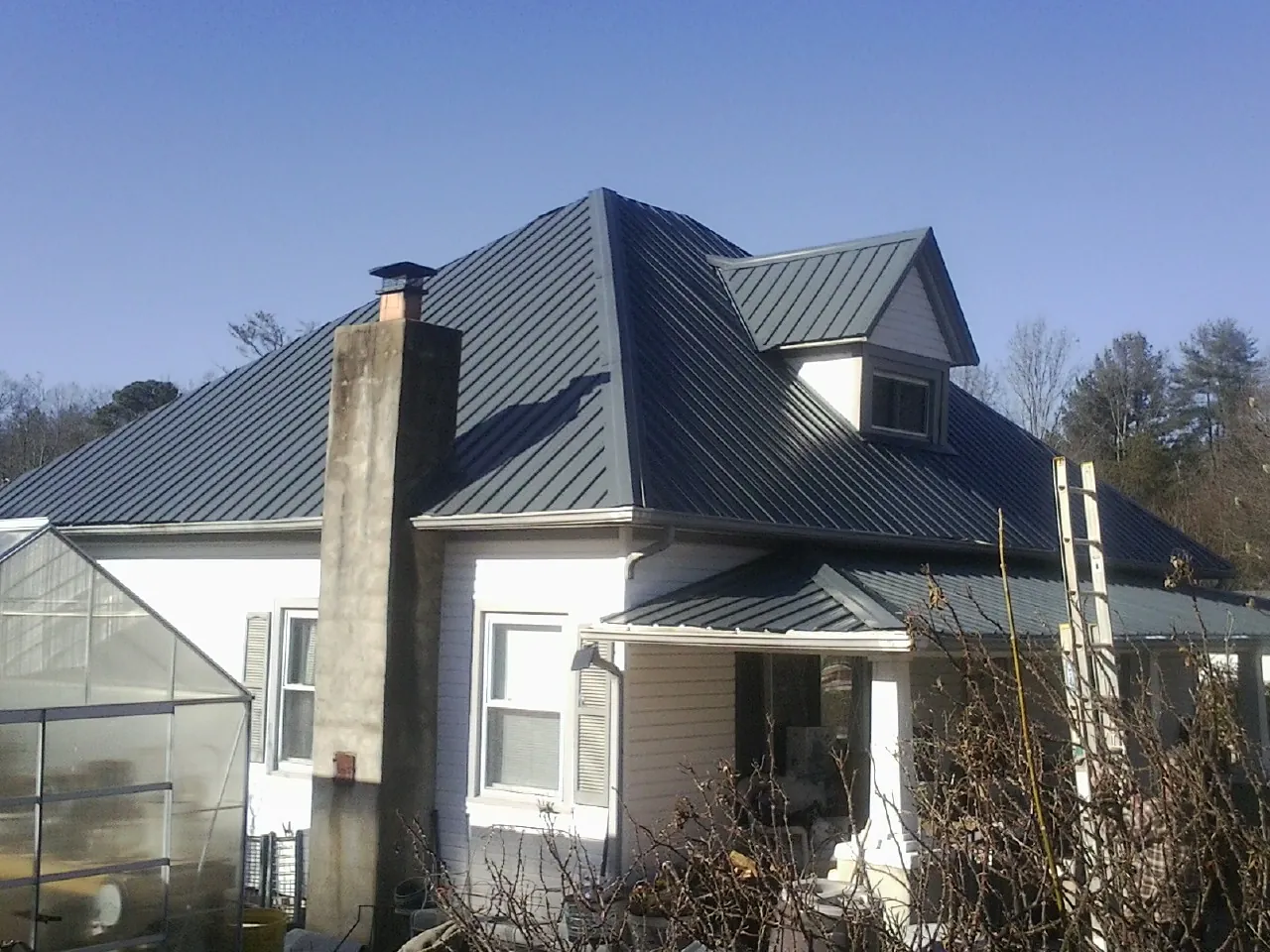 Dark blue standing seam metal roof on a white farmhouse with dormer — Slate & Tile Roof Repair by Roofing Brothers in Castle Creek