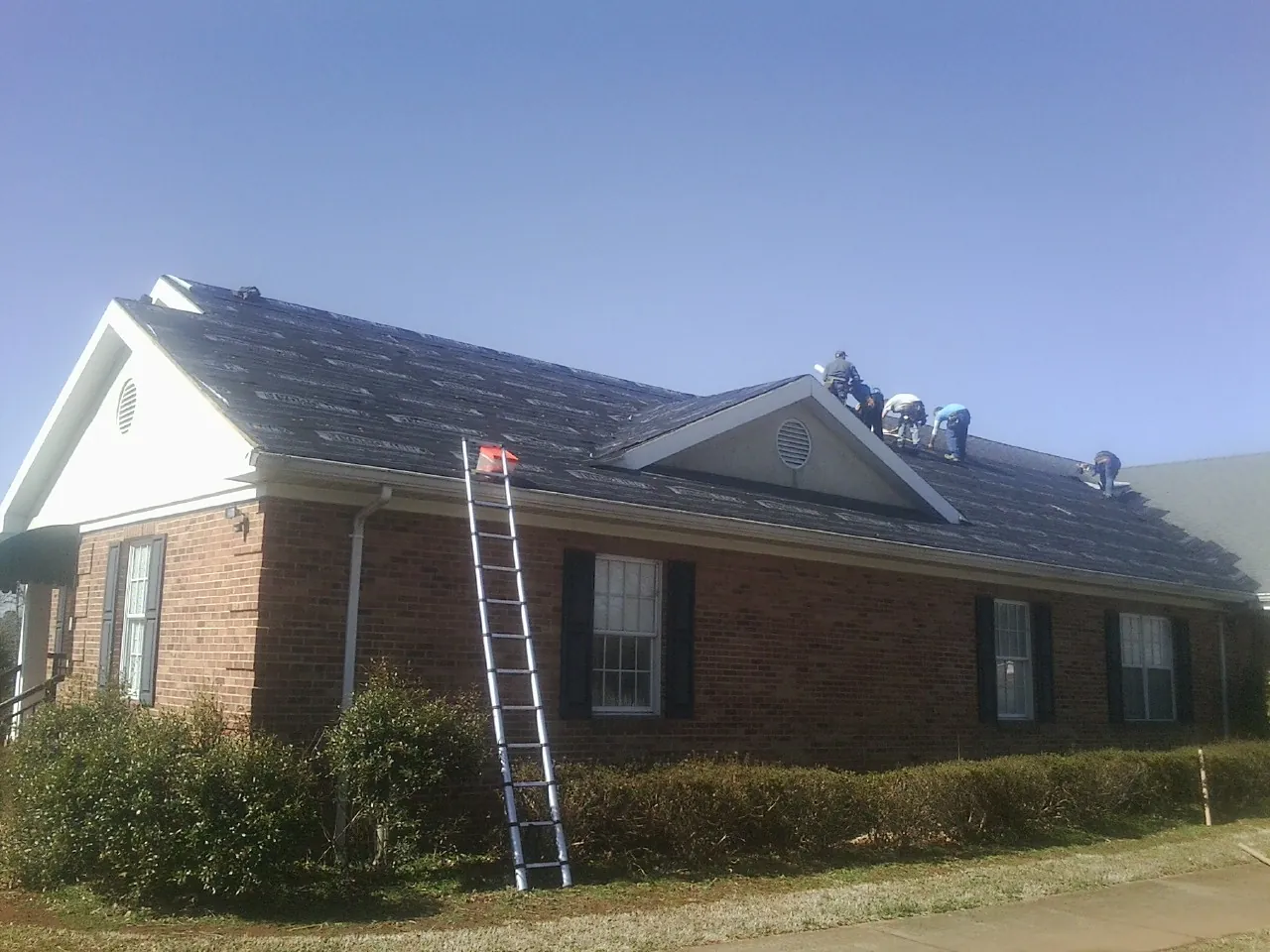 Crew tearing shingles off a brick ranch roof with a ladder set — Emergency Roof Repair work by our crew in Castle Creek