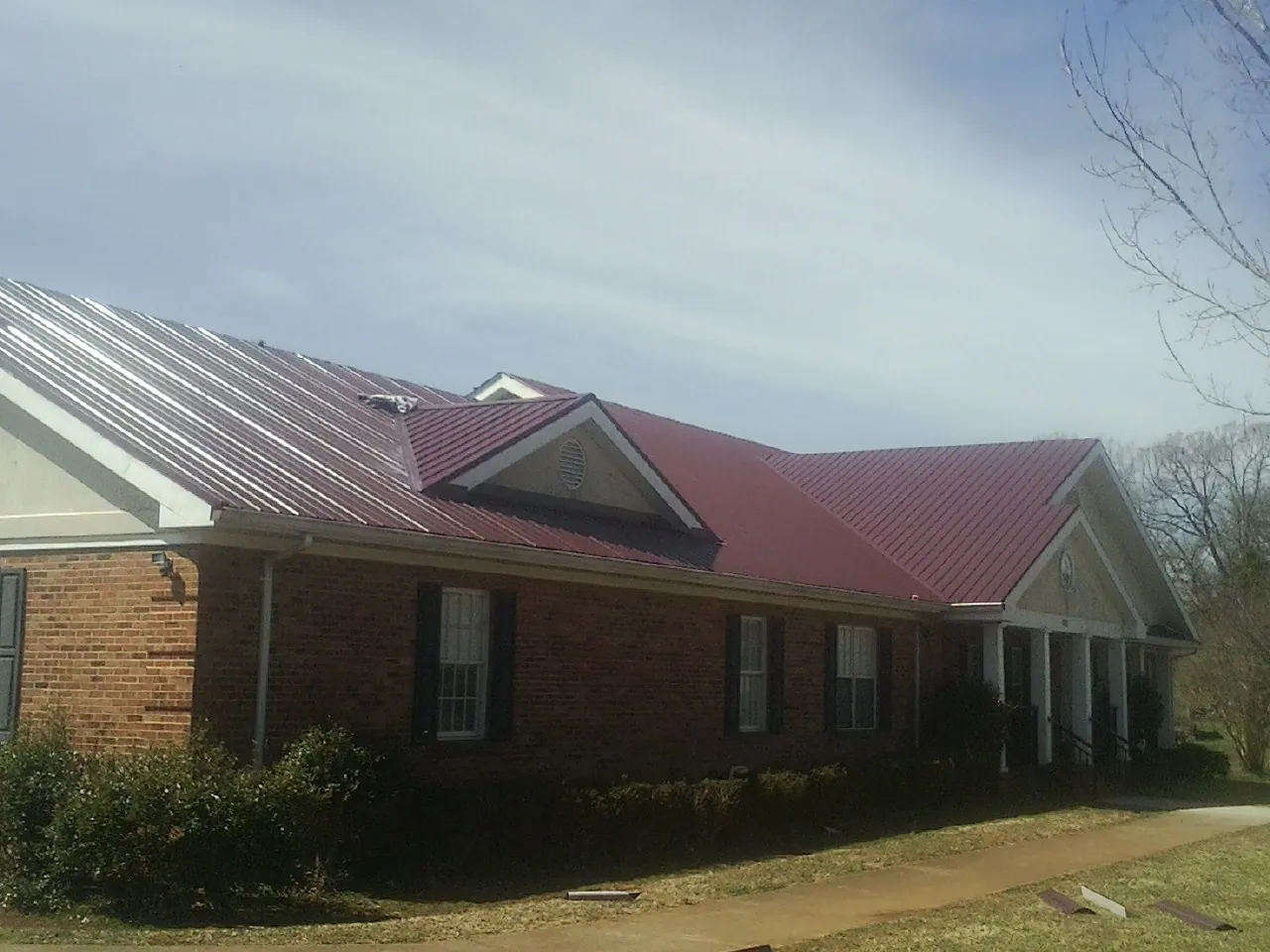 Red metal roof with gabled entries on a long brick building, from a Hail Damage Roof Repair job in Castle Creek