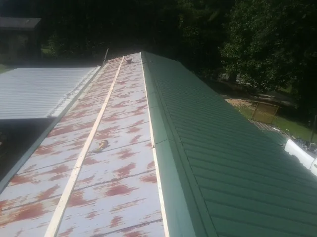 Old rusted panels beside newly installed green metal roofing — Wind Damage Roof Repair by Roofing Brothers in Castle Creek