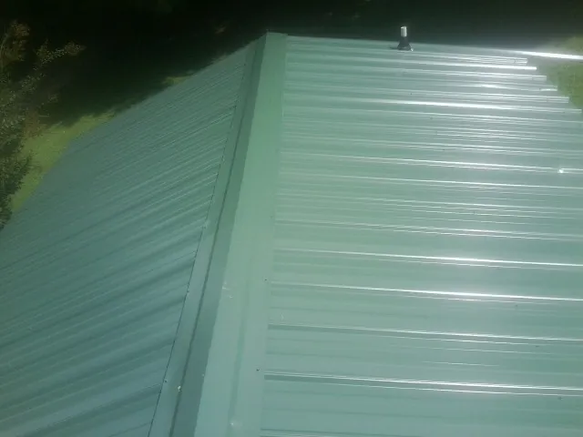 New green metal panels meeting at the ridge of a roof — Flat Roof Repair work by our crew in Castle Creek