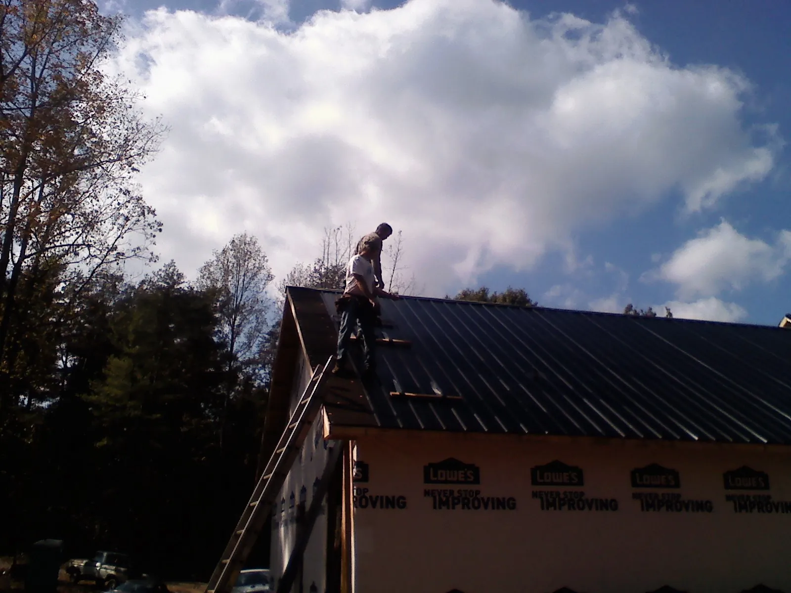 Roofer fastening dark metal panels high against a cloudy sky, from a Roof Inspection job in Castle Creek