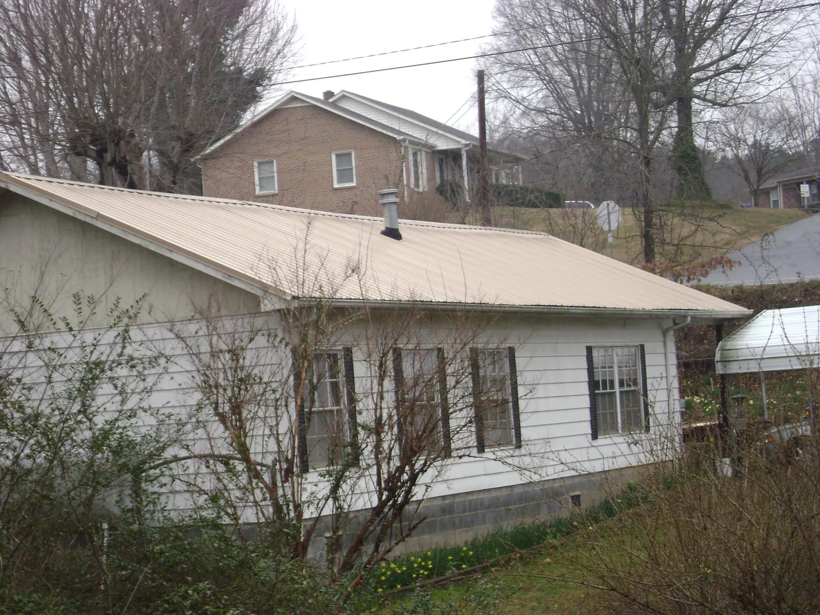 Tan metal roof on a white sided house set into a hillside — Commercial Roofing by Roofing Brothers in Castle Creek