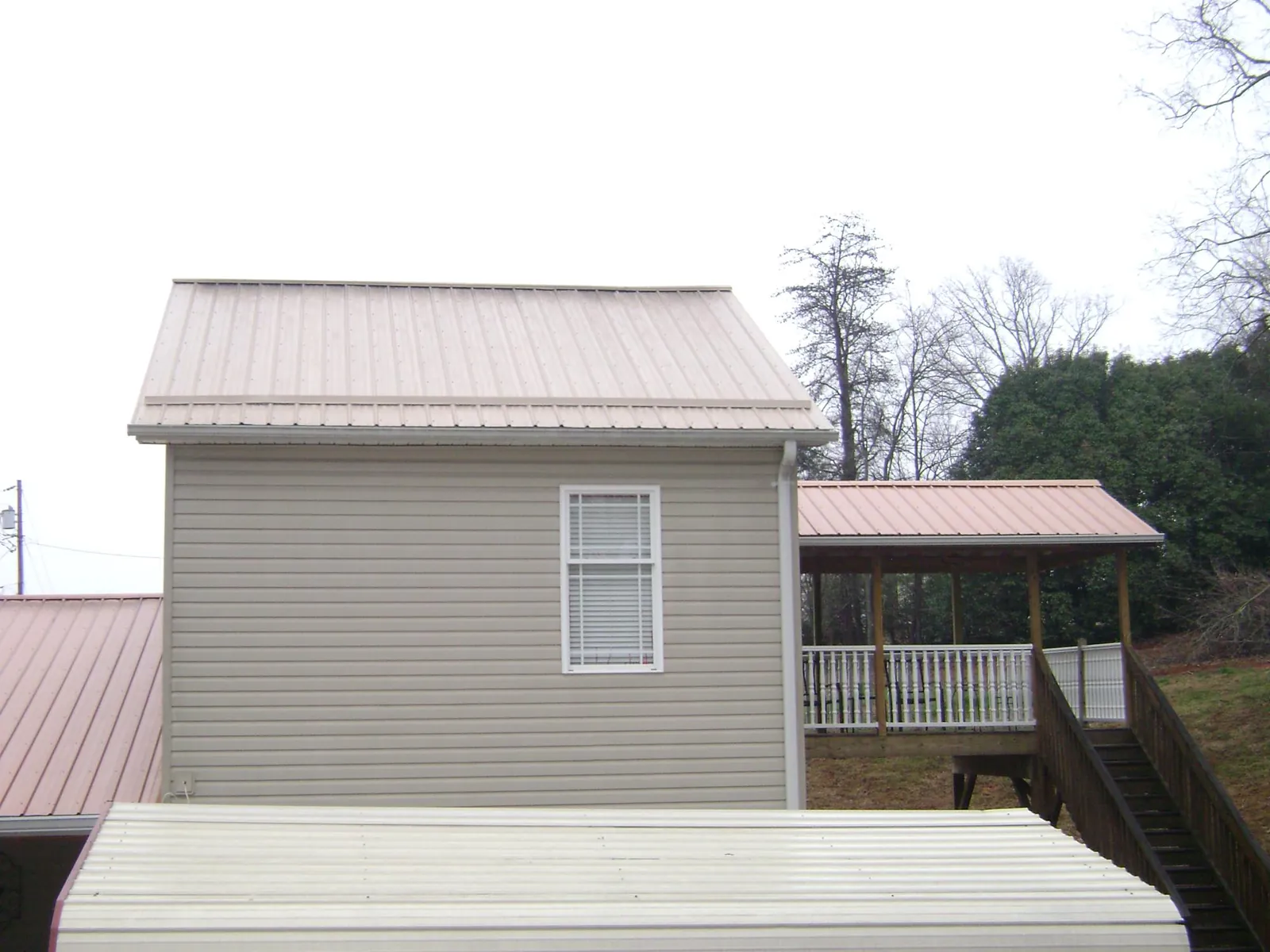 Tan metal roofs on a two story addition and attached porch, from a Roof Replacement job in Castle Creek